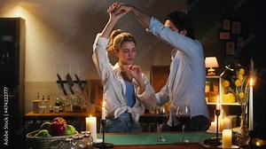 Man and woman dancing in cozy kitchen, romantic date dinner. Young husband and wife drinking red wine in evening. Loving couple, happy family relationships. Celebrating Valentine's Day together.