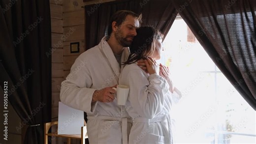 Mature couple in a white bathrobes hugging each other kissing at home bedroom. Intimate Moment. Tender embrace shared between a loving middle age man and woman, husband and wife. Deep love. Vacation