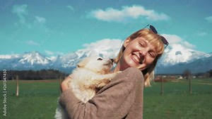 A young blonde woman is holding a white shepherd dog breed puppy her arms. Dog licks and bites her pretty face — cuteness overload.
