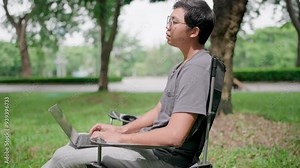 Programmer is writing code, typing on laptop keyboard. Programmer in casualwear developing new software writing program code on a laptop, work stress, working online, anxiety, working in a park.