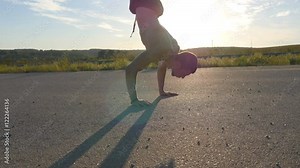 Young strong man showing impressive strength, doing a handstand outdoor. Fit muscular male fitness guy doing stunts on country road at sunset. Athlete training performs a handstand at muscle.Lifestyle