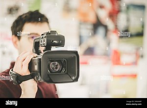 Male cameraman is holding a professional video camcorder, blurry background Stock Photo - Alamy