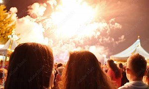 Slow motion video of fireworks exploding in vibrant hues above a festival crowd, with people’s faces lit up by the glow, capturing their excitement and wonder