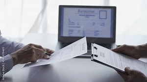 A hiring manager interviews a woman at a job interview to discuss a resume. of young man giving resume or cover letter to human resources manager during job interview in office