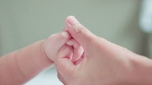 Close up hand of Cute baby newborn hand cuddle mother finger. Mom uses thumb finger playing, touch skin baby tender with love. Happy family, little innocent new infant adorable. Mother's Day concept.