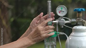 Elderly woman holding flow regulator with oxygen cylinder