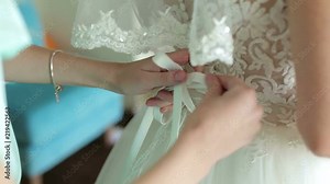 Corset wedding dress close-up. Preparation of the bride. Bridesmaid tying bow on wedding dress. Bride in the white dress. Bridesmaid helps fasten a wedding dress the bride.