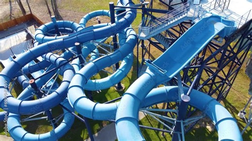 A complex blue water slide structure at an outdoor park surrounded by grass.
