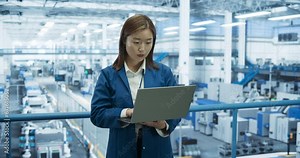 Japanese Factory Specialist Working on Laptop at a Futuristic Industrial Manufacturing Plant. Project Manager Monitoring Business Data on a Computer, Checking Reports and Planning Research