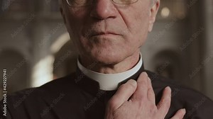 Close up of old Caucasian pastor wearing black shirt and white collar standing in Lutheran church and fixing his collar