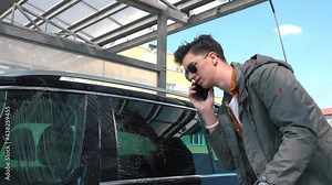 Urgent call. Wash dry dirt off the surface man talking on phone and washes the car with a brush multitasking of an active entrepreneur. Hand wash glass of cars.