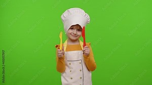 Little charming child girl dressed in apron and hat like chef cook with plastic fork and knife, waving head approval on chroma key background. Nutrition, family cooking school, children education game