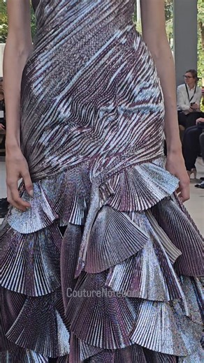 Let's talk about this fabric: a jacquard lamé enriched with silk and lurex, pleated in two directions to catch and reflect light from multiple angles, giving it a bioluminescent appearance. Designer #ArdAzAei used this fabric to create handcrafted accordion pleats that wrap around the body in a spiral pattern. The design then transitions into a full organza skirt decorated with 70 individual pleated fans. | CoutureNotebook