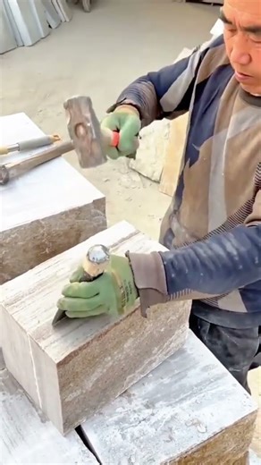 A stonemason is shaping a rectangular stone block with a hammer