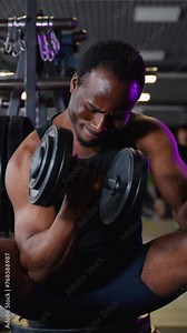 African man training biceps muscles with dumbbell in fitness gym. Vertical video