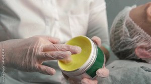 Women's hands of a cosmetologist take a yellow moisturizing, nourishing cream from a jar. Beauty salon. The profession of a cosmetologist.