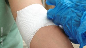 Video footage of a professional nurse demonstrating how to wrap a patient's arm with an elastic bandage during a home visit.