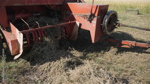 1960s: Bar pushes bales to side in bale accumulator machine. Tractor pulls accumulator with bales behind it. Tractor and accumulator drive over field as bales get pushed into place.