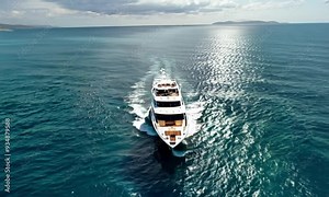 An aerial view of a luxury yacht cruising through the open sea with a scenic coastline in the background.