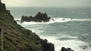 Stormy rough seas and breaking Atlantic ocean waves over rocks at Lands End Cornwall, UK after Storm Bella gale force winds surge through the coastline.
