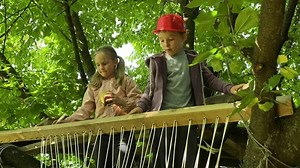 Family bonding. The joy of childhood by spending leisure time together in the great outdoors. Dad and elementary age kids joyfully build a summer treehouse, creating delightful childhood memories.