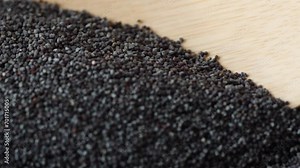 opium poppy seeds from a wooden spoon fall down.slow motion.poppy macro heap harvest