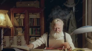 Elderly writer smoking cigarette, taking notes and reading over his manuscript, then crumpling and discarding paper in frustration as working at desk in cozy study