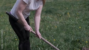 Woman digging into the ground with a hoe, showcasing slow motion movements in a garden setting during daylight