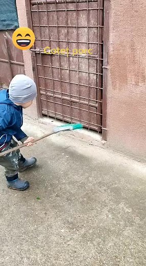 Child Sweeping Outside in Blue Jacket and Camouflage Pants