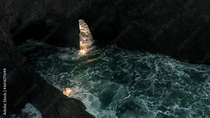 Aerial: Sun shining through open hole in a cliff with waves crashing through it. Greenwood Creek State Beach at Elk on the Mendocino Coastline. USA