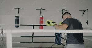 Slow motion of young sportsman in outfit boxing in ring alone wearing gloves concentrated on shadow fight. Sports and workout concept.