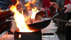 Professional Chef in a Commercial Kitchen Cooking Flambe Style. Chef frying food in flaming pan on gas hob in commercial kitchen.