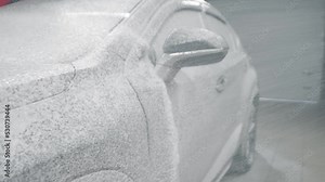 Cleaning the machine with active foam. Washing sedan car with foam and a high pressure water from front to back. Professional car wash indoors