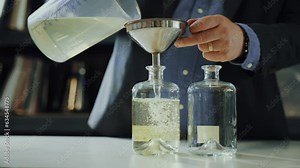 Male expert pouring distilled gin in a glass bottle with a funnel, quality control process in a gin distillery production
