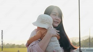 Asian mother walking while carrying newborn son infant, carry up baby, autumn family time, warmness of mommy love, beautiful sunlight during sunset, child health insurance, human population growth