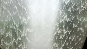 Powerful flow of waterfall, closeup. Background from wave nature water stream, macro view. Tropical pattern for relax. Big fountain falling from the roof to floor. Camera tilt down.