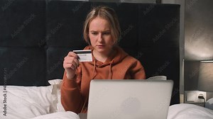 Woman doing online shopping using laptop and credit card while laying on bed.