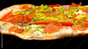 Pizza rotates on a black background, side view, close-up. Pizza with toppings, salami, tomatoes, fresh onions, ham, olives, peppers, cheese. Fast food.