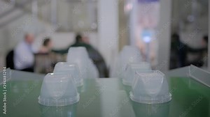 Stack of polypropylene food containers on conveyor belt of automatic plastic injection molding machine with robotic arm at exhibition, trade show. Manufacturing, industry, automated technology concept