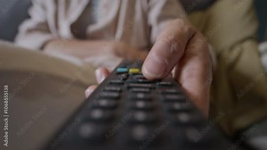Closeup of unrecognizable woman holding remote control and pressing buttons, switching channels while watching TV at home