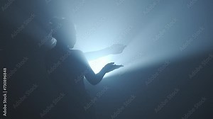Silhouette in lighting concept. Female model against bright lantern and smoke on black background in studio. Female silhouette standing surrounded by light beams and covering the light with hands.