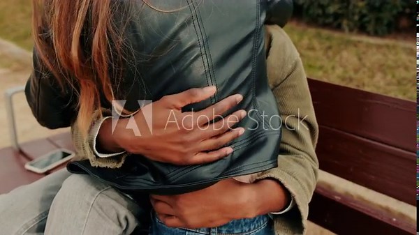 Two women, a lesbian couple or best friends, hug on a park bench during a crisp autumn day. This video evokes feelings of love, friendship, and togetherness.