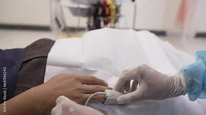A medical professional in protective gear attaches a pulse oximeter to a patient's finger, monitoring oxygen levels and ensuring proper healthcare diagnostics.