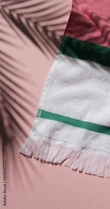 Vertical video of colorful striped cotton beach towel on the pink background with moving palm leaves shadows. Copy space