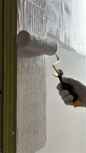 applying gray textured paint to a wall using a paint roller tool for home renovation activities