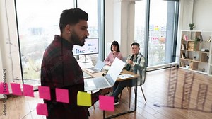 Group of colleagues conducting brainstorming session in modern office using sticky notes and digital charts. Team members discussing ideas, collaborating on project planning and strategies.