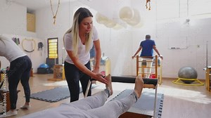 Older woman exercising in Pilates Studio Session. An elderly caucasian person laid on Machine stretching body with the guidance of Coach instructing exercise
