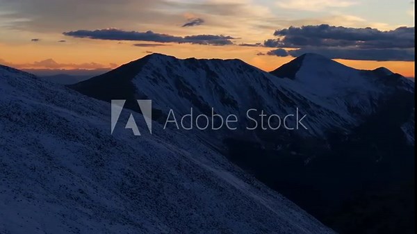 Glowing Rocky Mountains sunset Mt Mount Shavano Elbert Huron La Plata Tabeguache Antero Peak Colorado aerial drone fall autumn snow Sawatch Range top of summit sun on horizon clouds pan right motion