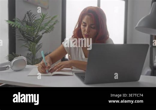 Woman writing in notebook with turquoise pen and laptop at desk in building; concentration productivity Stock Video Footage - Alamy