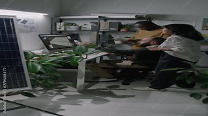 Side full vertical footage of multiethnic team of renewable energy engineers negotiating ideas about new solar panel mockup on computer screen during workday in modern loft office